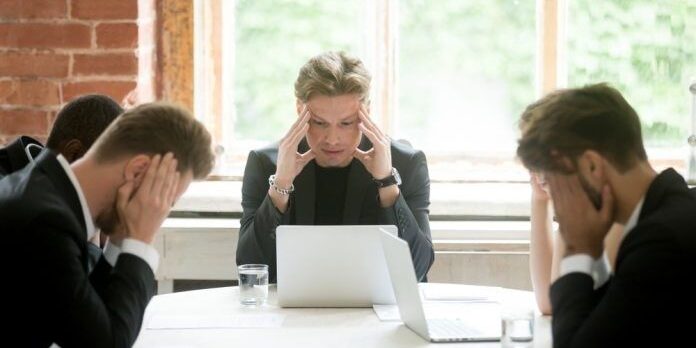 selected-01-crisis-management-team-meeting-optimized Pressat möte där fyra personer sitter med händerna mot huvudet