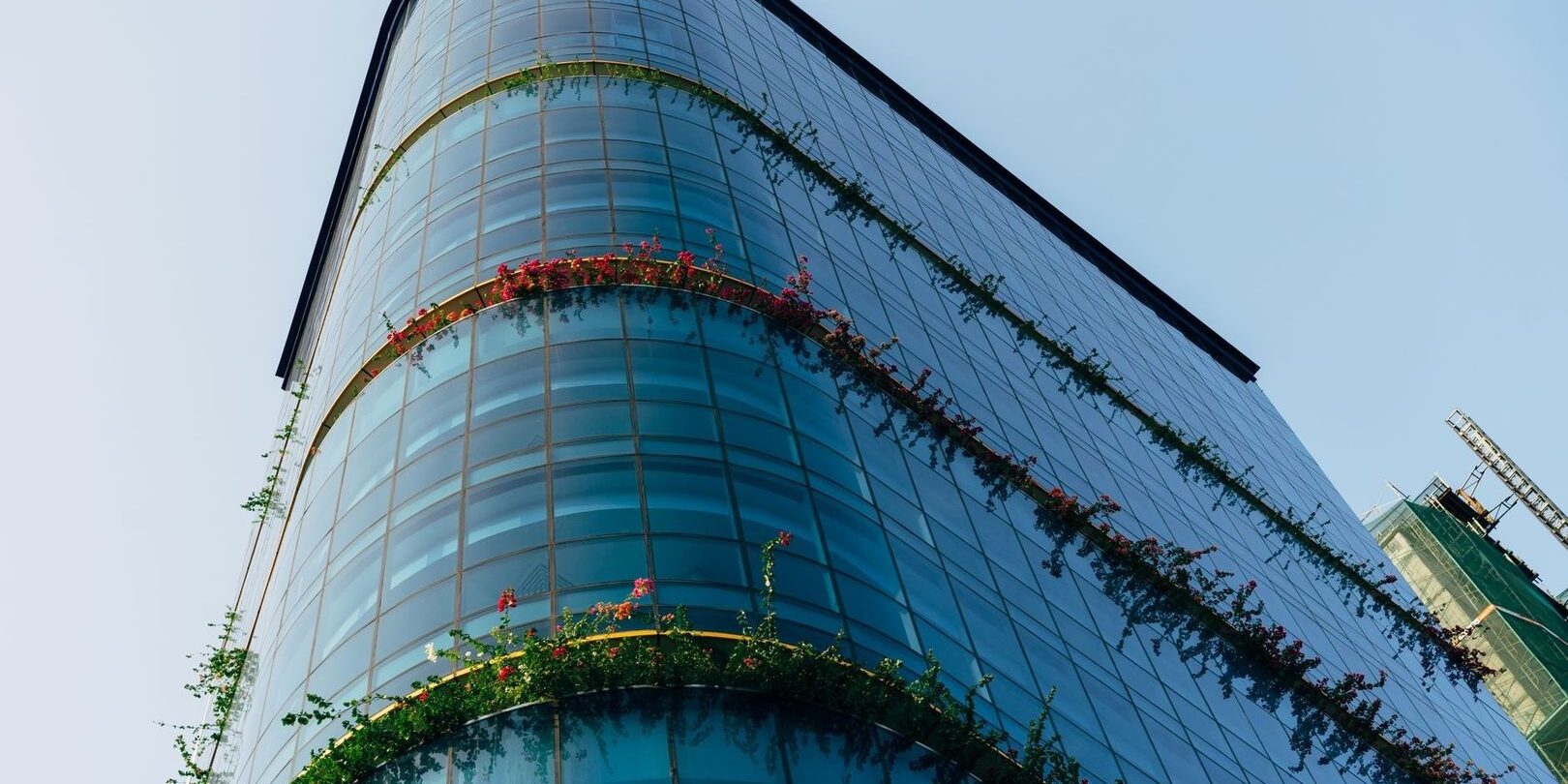 selected-01-transparent-corporate-sustainability-rep-optimized Glasfasad med växtlighet och blommande terrasser mot blå himmel